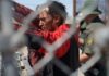 Individual at a border fence with law enforcement officers nearby