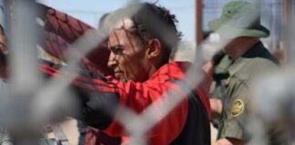 Individual at a border fence with law enforcement officers nearby