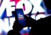 A person holding a smartphone displaying the Fox News logo against a colorful background