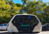 An autonomous shuttle vehicle parked on a city street surrounded by trees