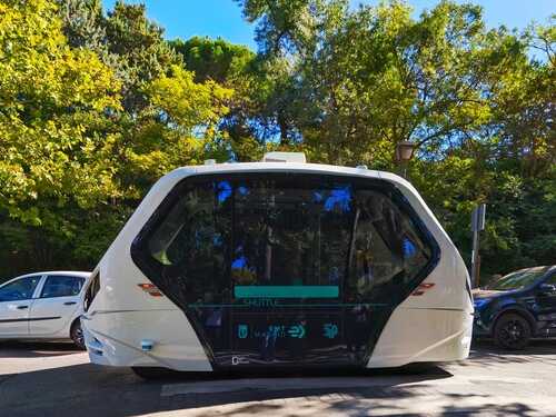 An autonomous shuttle vehicle parked on a city street surrounded by trees