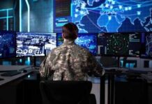 Military personnel monitoring multiple screens in a command center