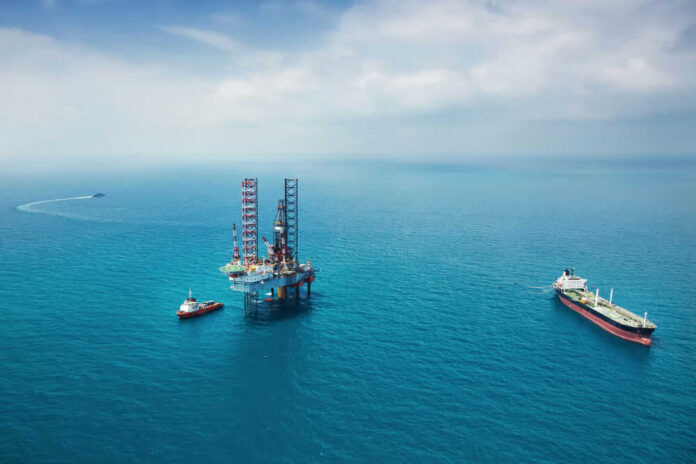 Oil rig surrounded by ships in the ocean.