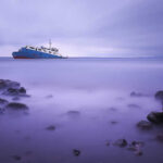 Ship on calm sea with rocky foreground