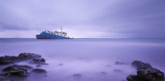 Ship on calm sea with rocky foreground