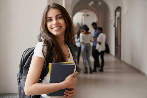 Smiling student holding books in a school hallway