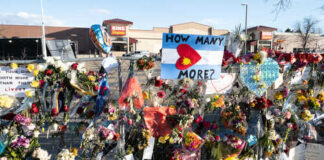 A memorial with flowers and signs expressing grief and questions about gun violence