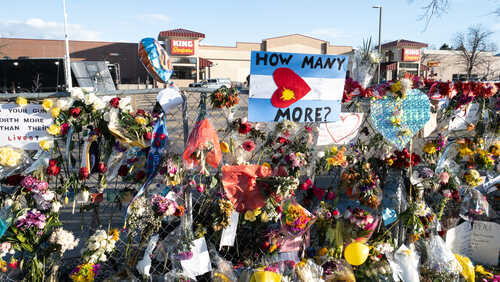 A memorial with flowers and signs expressing grief and questions about gun violence