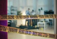 Police crime scene tape blocking an area with investigators in the background