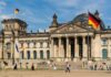 The Reichstag building in Berlin with German flags and people walking in front