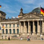 Merkel Strikes – Merz Cornered The Reichstag building in Berlin with German flags and people walking in front