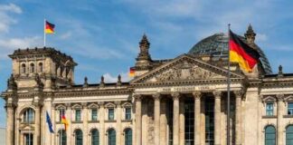 The Reichstag building in Berlin with German flags and people walking in front