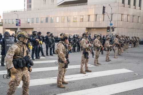 Military personnel and law enforcement officers lined up in an urban area